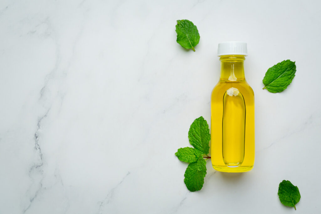 Bottle of yellow oil with fresh mint leaves on a white marble surface.