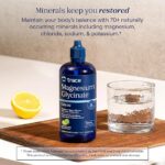 Blue bottle of Trace Magnesium Glycinate liquid supplement on a wooden board beside a lemon half and a glass of water.