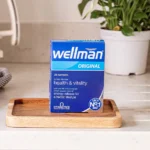 Blue Wellman Original vitamin box on a wooden tray in a bright kitchen, promoting health & vitality text visible on front.